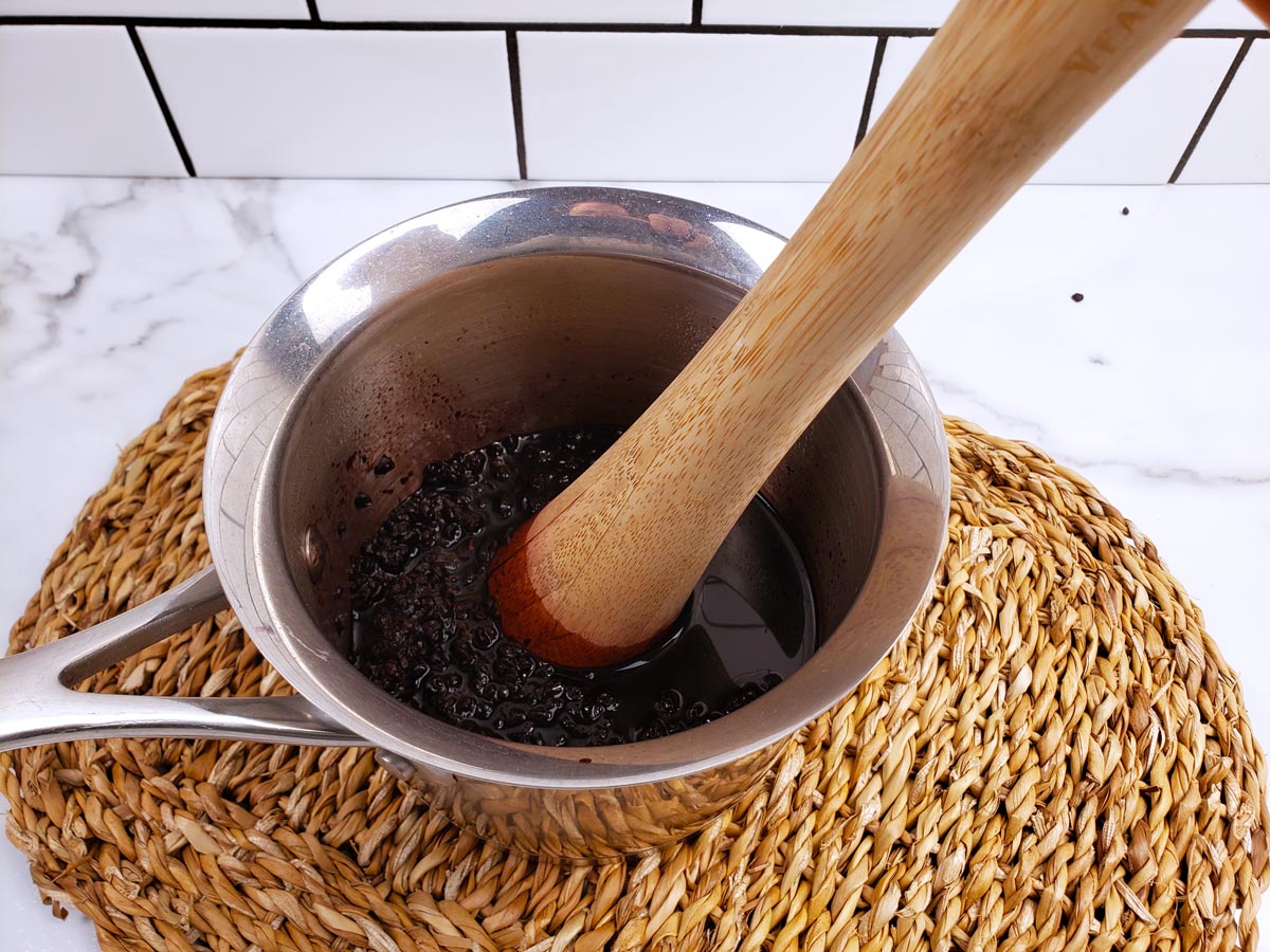 Elderberries being mashed with a kraut pounder.