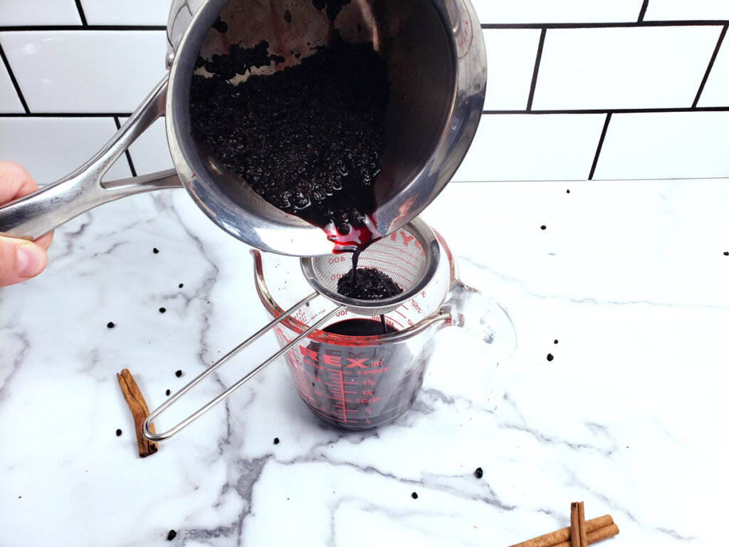 Elderberry juice being poured into a strainer.