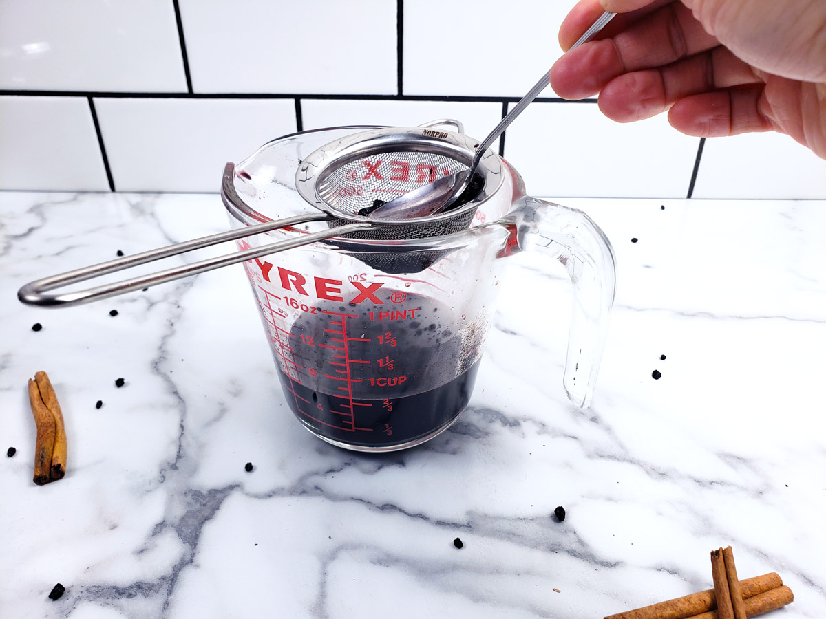 Elderberry juice being strained through a stainless steel strainer.
