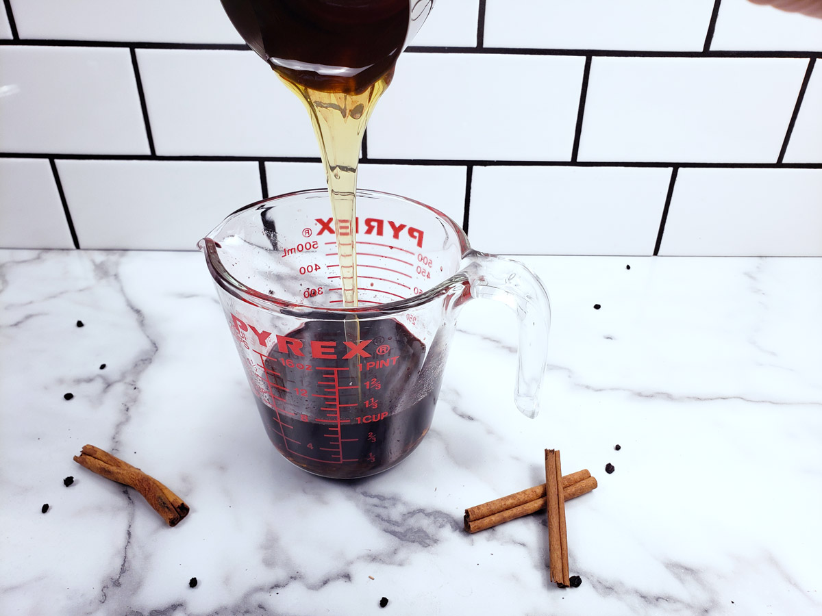 Honey being added to a measuring cup filled with elderberry syrup.