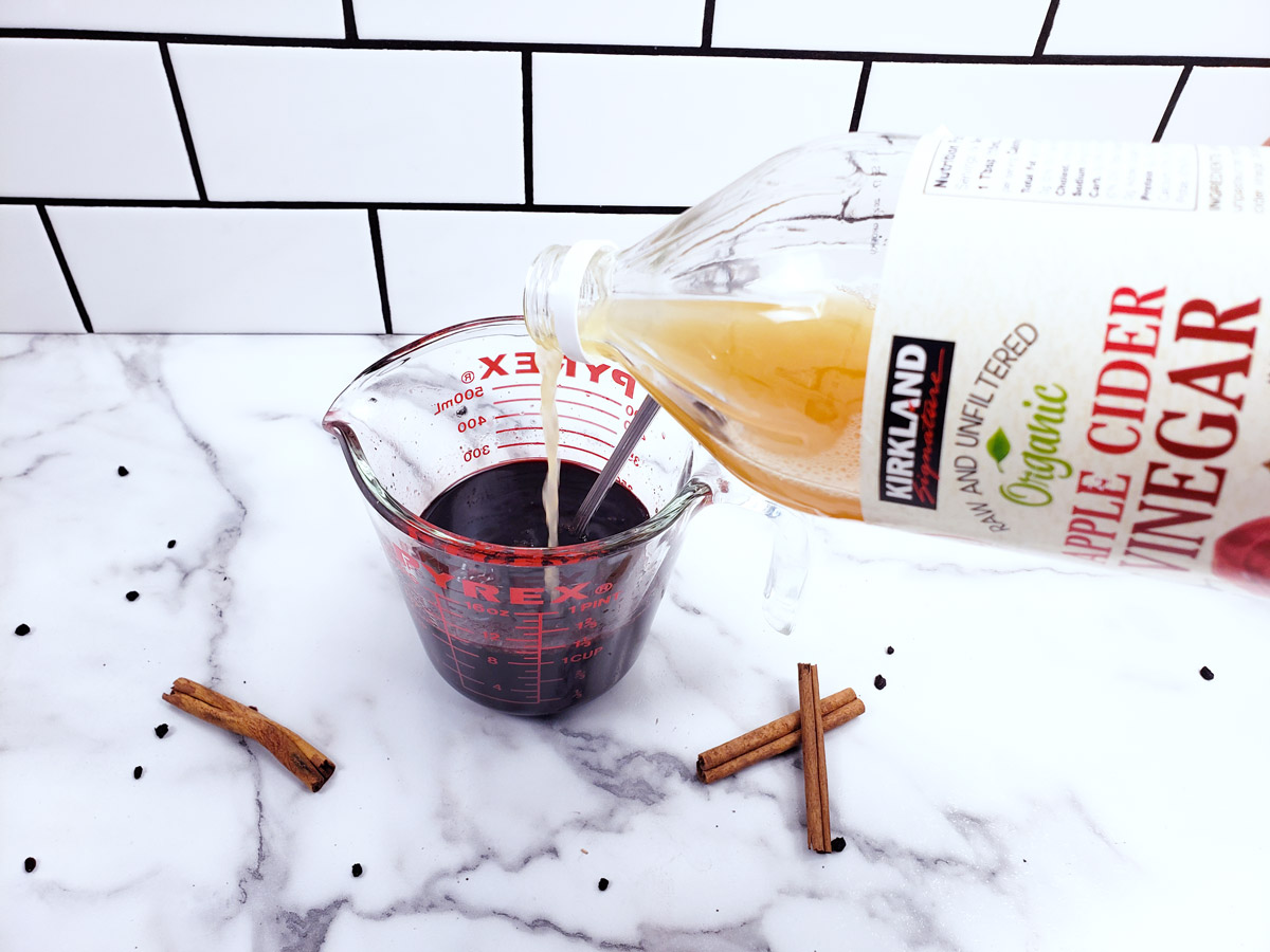 Apple cider vinegar being added to a measuring cup of elderberry syrup.