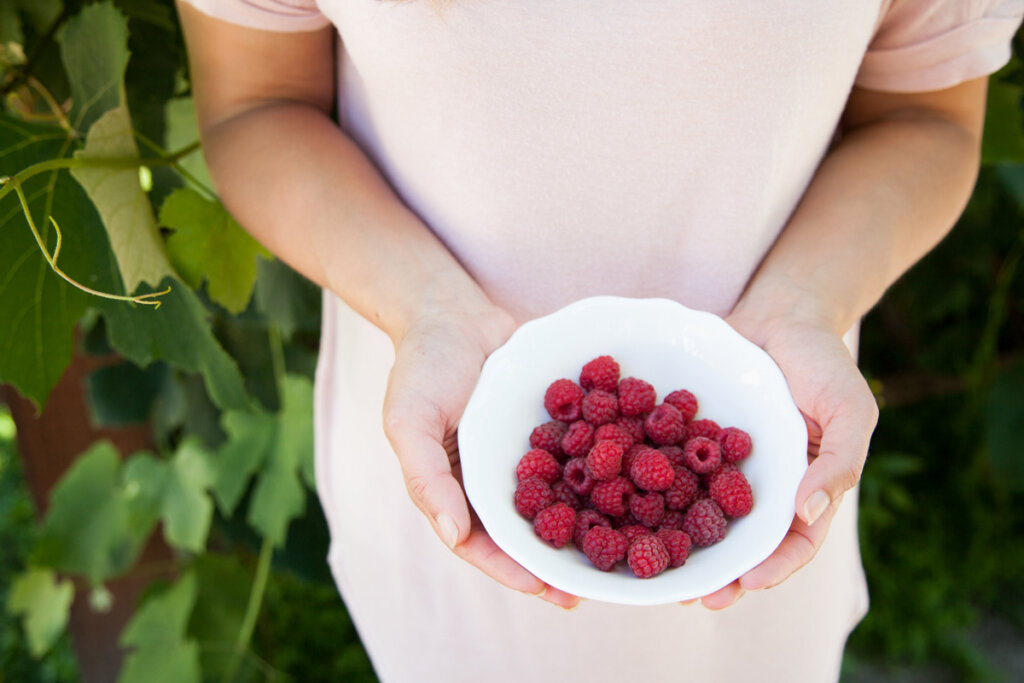 A woman holding a white bowl full of raspberries.