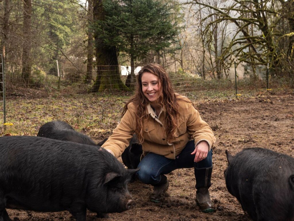 A woman squatting next to american guinea hogs.