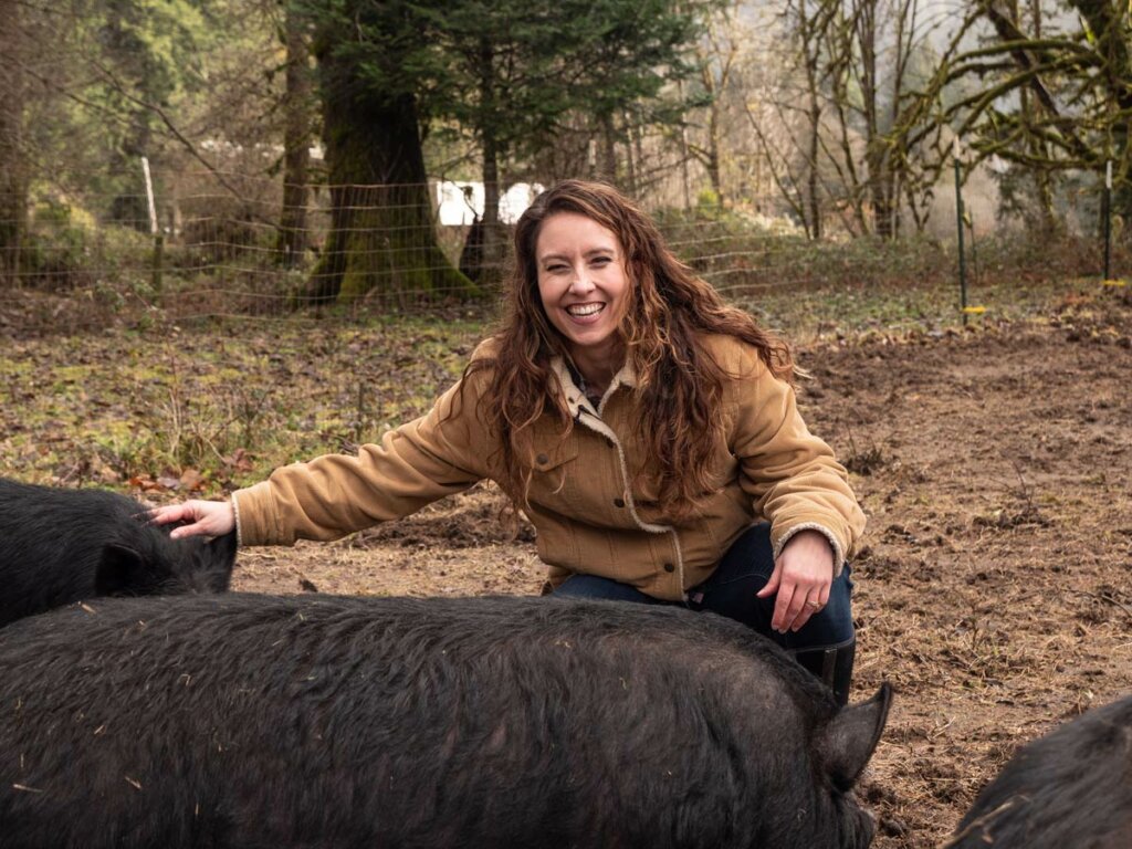A woman smiling while petting her american guinea hogs.