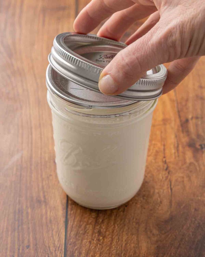 A hand placing a lid on a jar of homemade buttermilk.