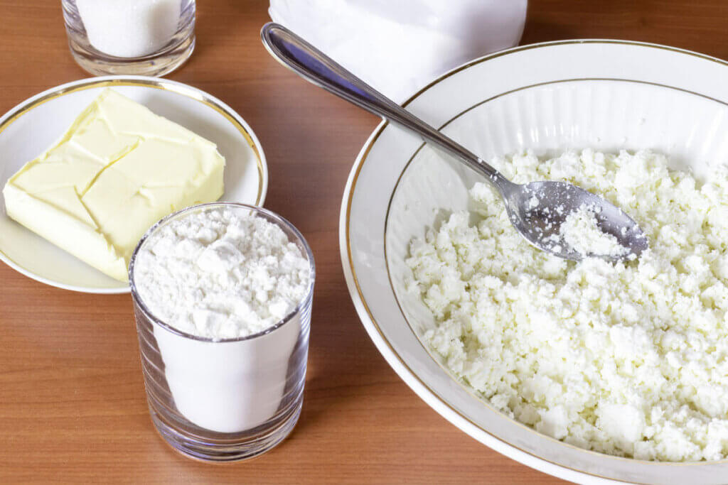 A bowl of crumbled cheese and a small glass of yogurt with other fermented milk products on a wooden table.