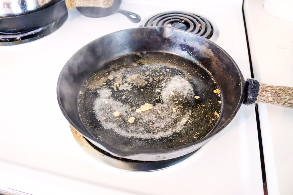 A cast iron skillet with a small layer of water inside simmering on the stove to loosen stuck on food.