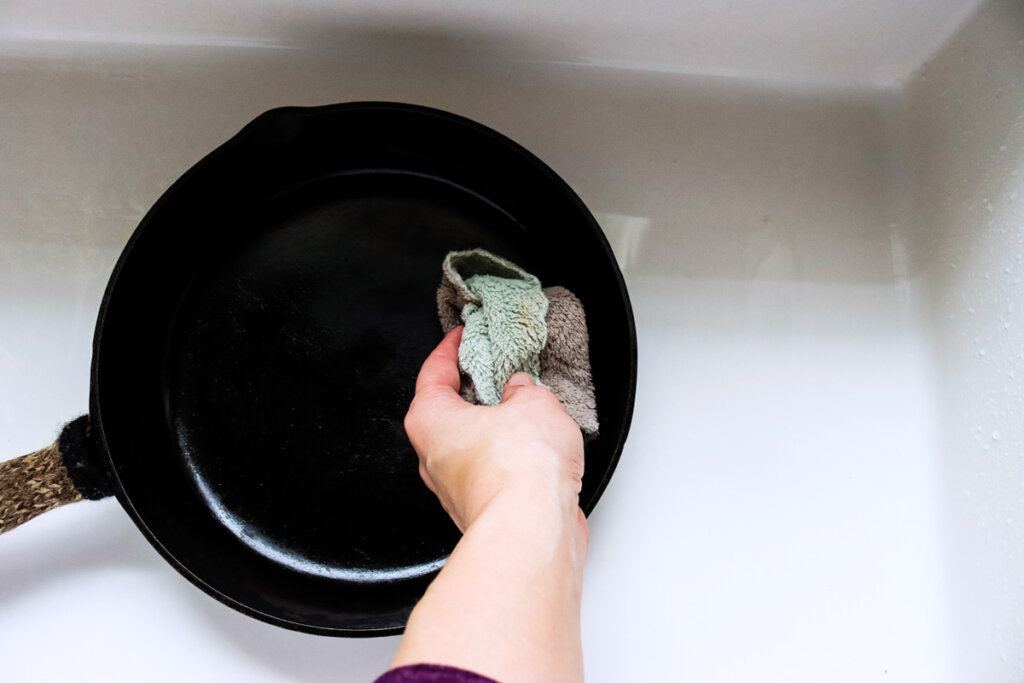 A woman's hand wiping out a cast iron skillet with a paper towel.