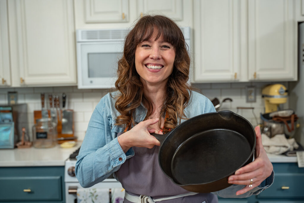 A woman standing in the kitchen holding a cast iron skillet up.
