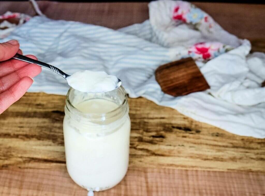 A spoon scooping buttermilk out of a mason jar.