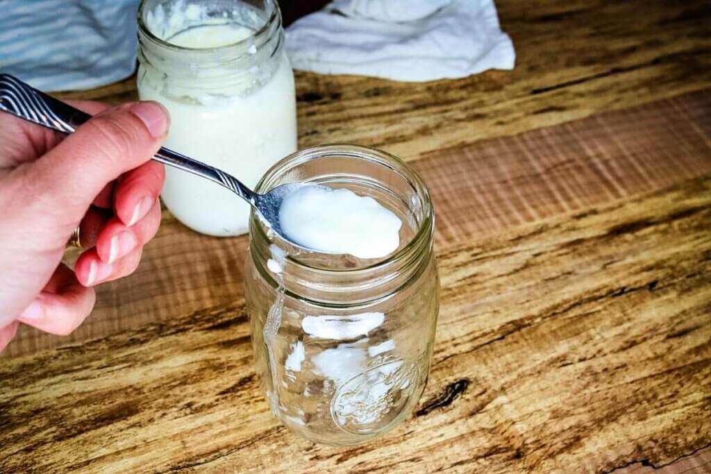 A spoon of buttermilk being poured into a jar.