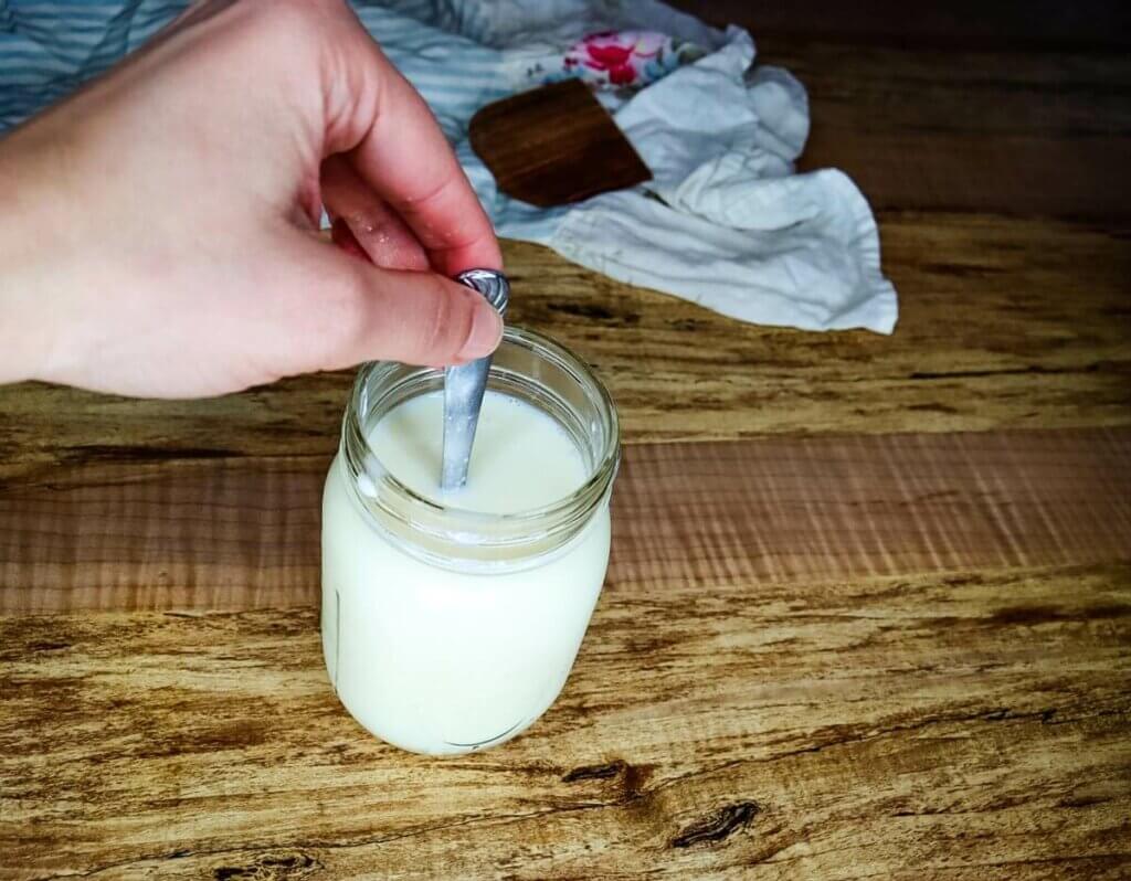 A spoon stirring cultured buttermilk into a glass of milk.