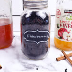 Pinterest pin for elderberry recipes with an image of elderberries in a glass jar.