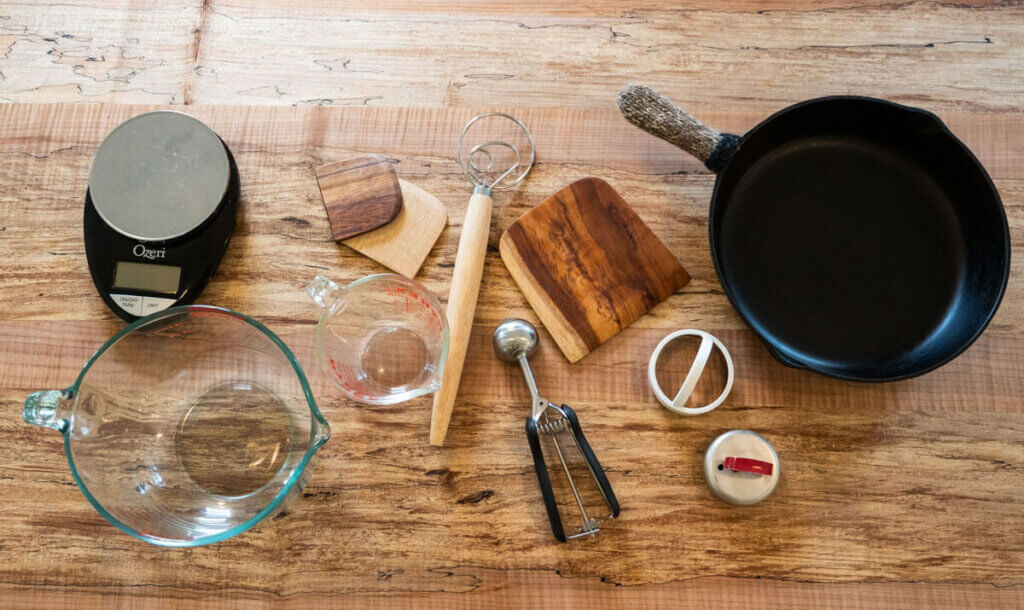 Image of 11 different kitchen tools sitting on a wooden counter top. 