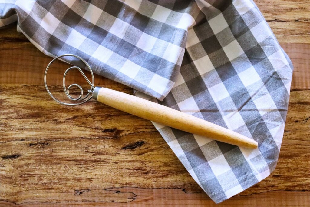 Danish dough whisk laying on a counter on top of a checkered dish towel.