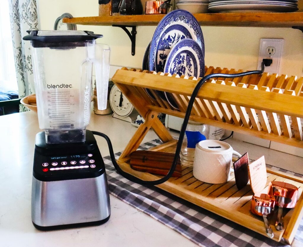 A BlendTec blender on the kitchen counter next to a wooden drying dish rack.