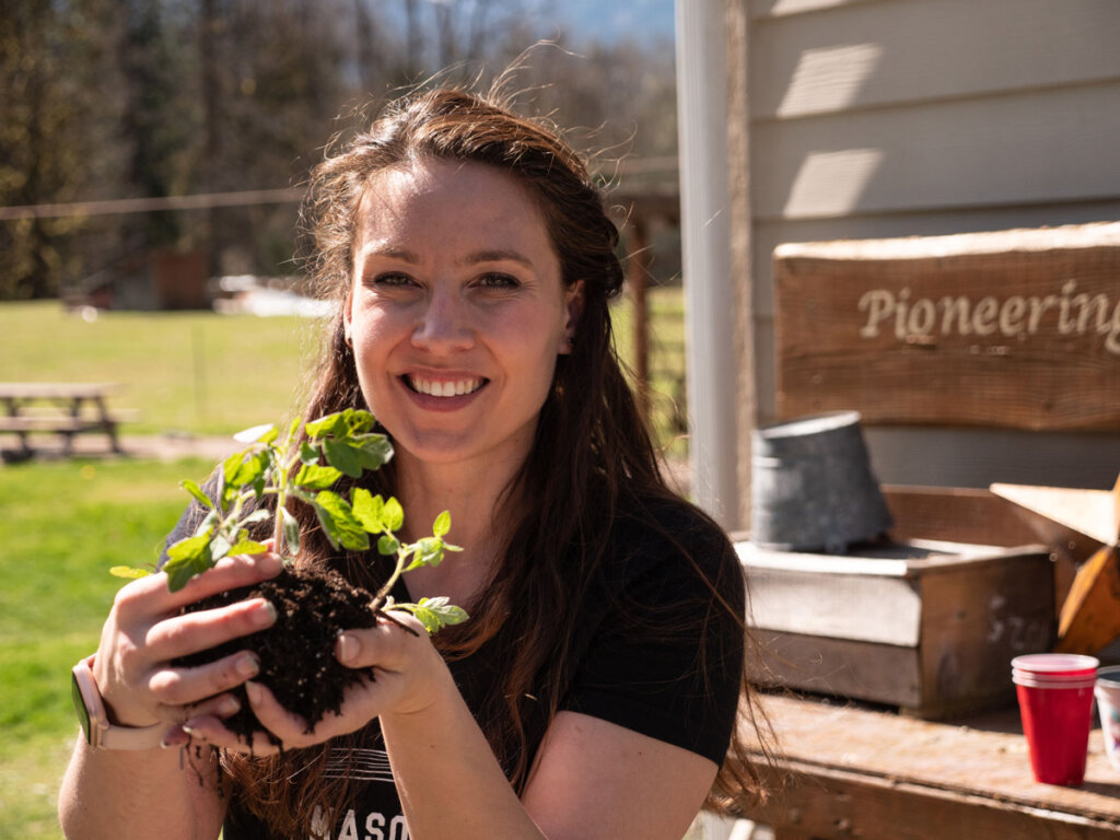 A woman holding seedlings in her hands, standing outside by a potting bench.