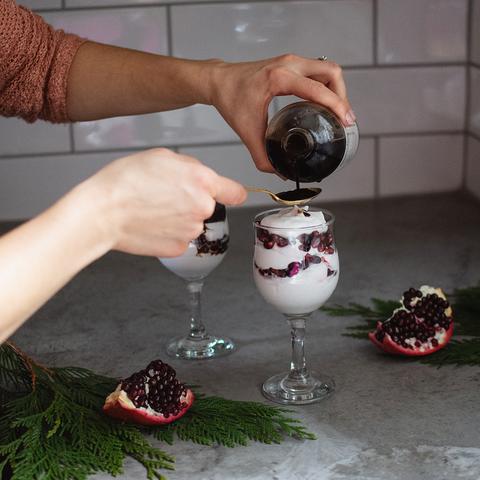 A woman pouring elderberry syrup onto a spoon with an elderberry fool on the counter.