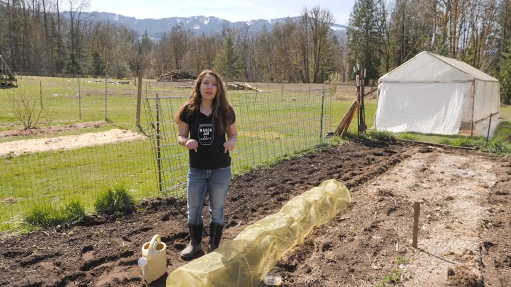 A woman standing in the garden next to a row cover protecting her crops.