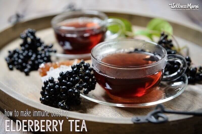 Two glasses of elderberry tea on a tray with fresh elderberry clusters.