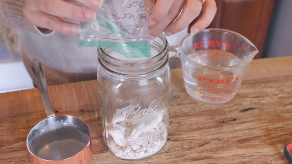 Image of hands pouring in dehydrated sourdough starter into a mason jar.
