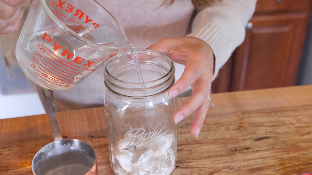 Image of hands pouring in warm water into a jar with dehydrated sourdough starter inside.