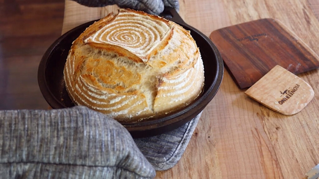 Image of a loaf of freshly made sourdough bread being placed onto a wooden counter.