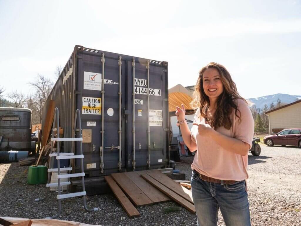 A woman standing in front of a shipping container pointing to it.