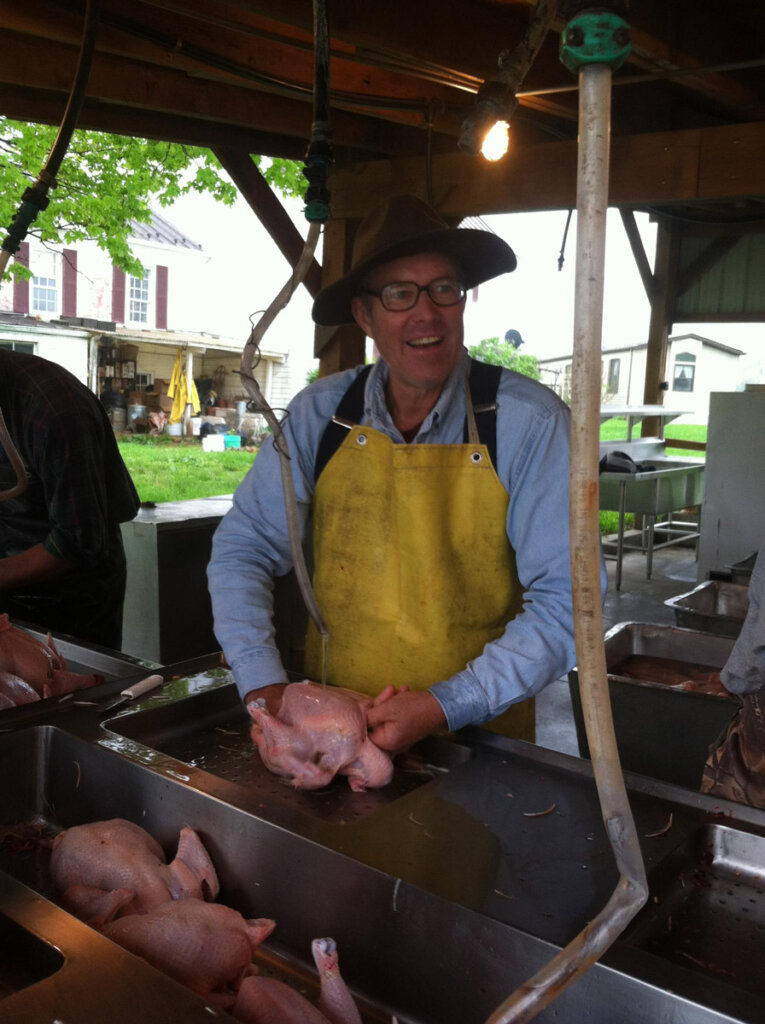 A man butchering a chicken in an outdoor kitchen area.