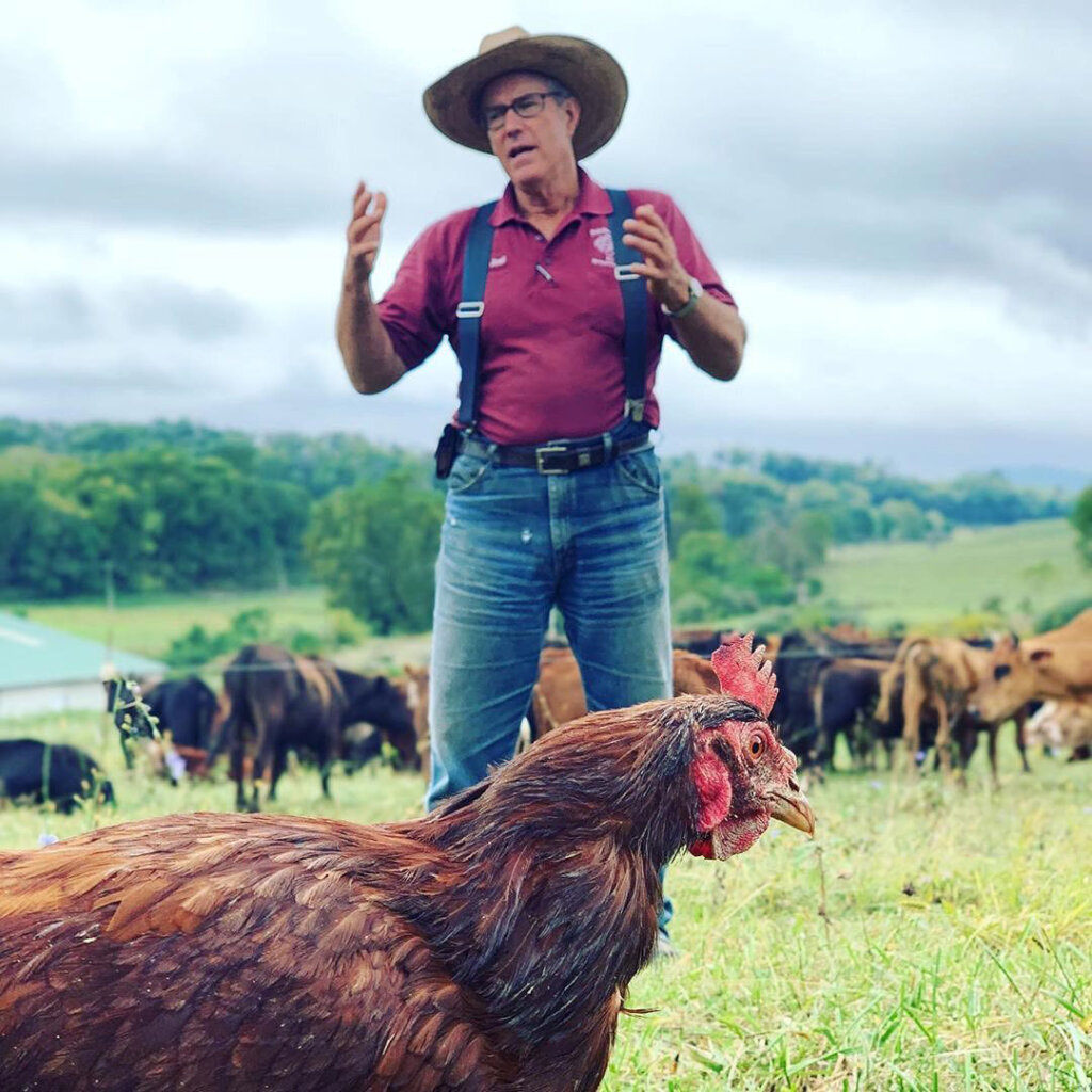 A man wearing a cowboy hat standing in a pasture of chickens and cows.