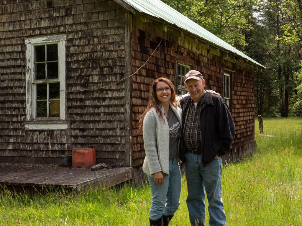 A father and daughter standing in front of an old farmhouse.