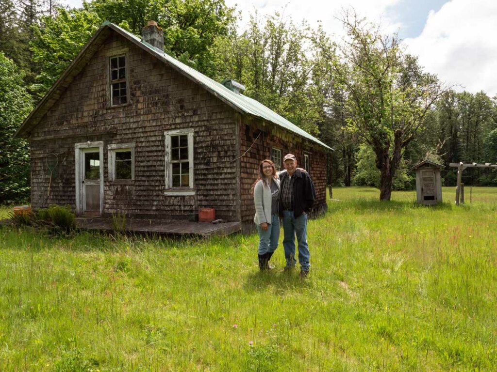 A father and daughter standing in front of an old farmhouse.