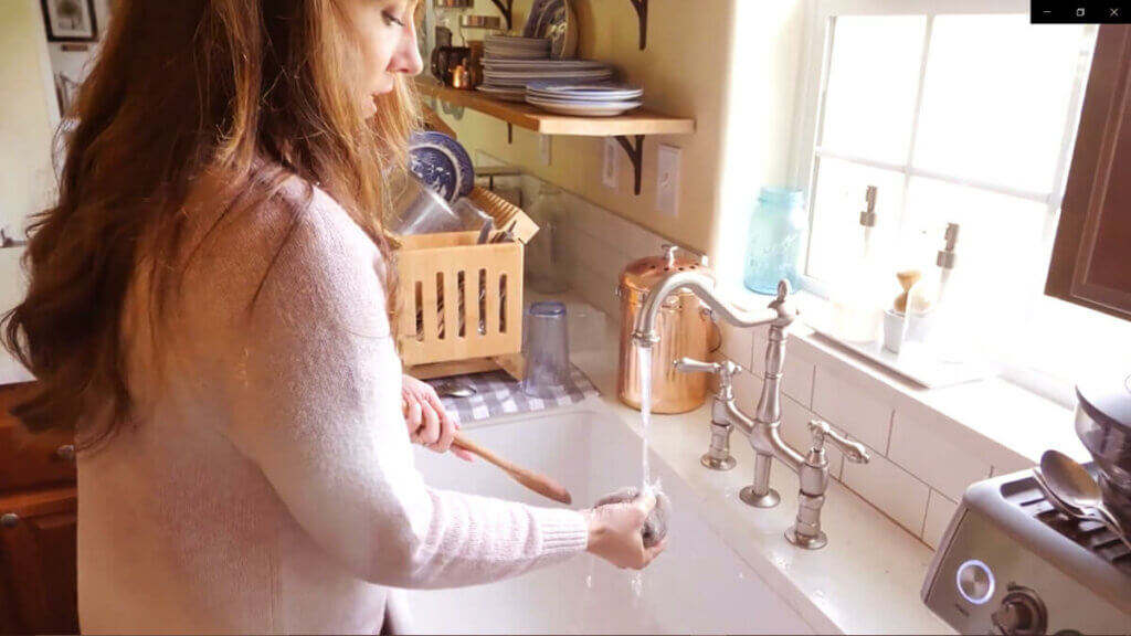 A woman rinsing off a wooden spoon in the kitchen sink.