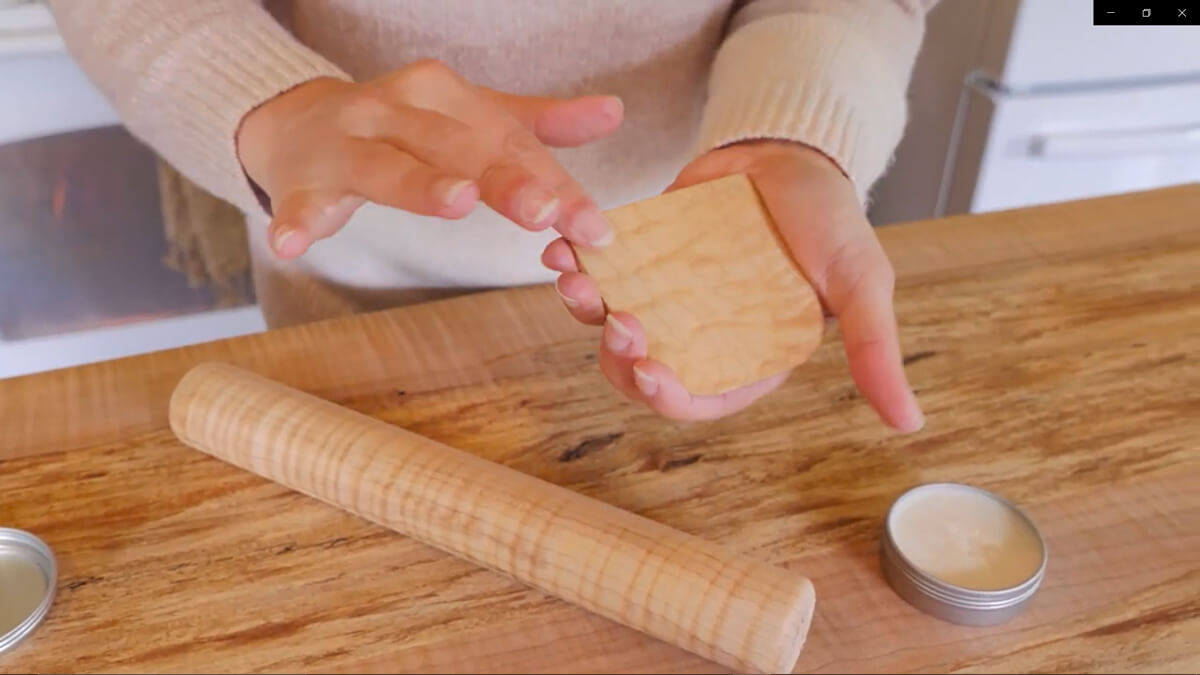 A woman conditioning a wooden dough scraper with wood butter and her hands.