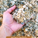 Pinterest pin for using woodchips in the garden. Image of a hand scooping up woodchips.