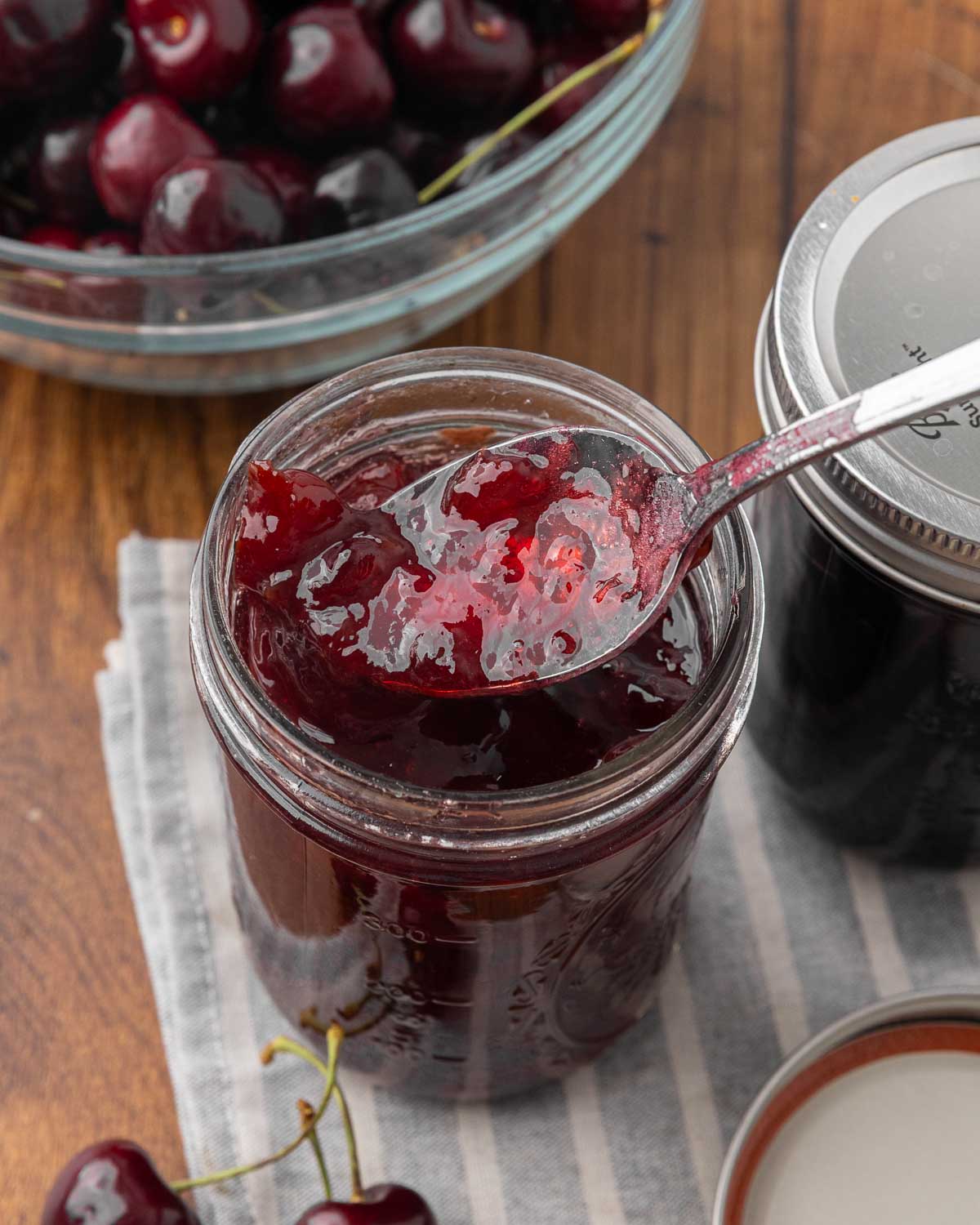 A spoon lifting a scoop of cherry jam out of a jar.