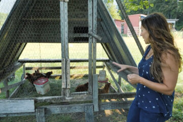 A woman standing beside a mobile chicken tractor with chickens inside.
