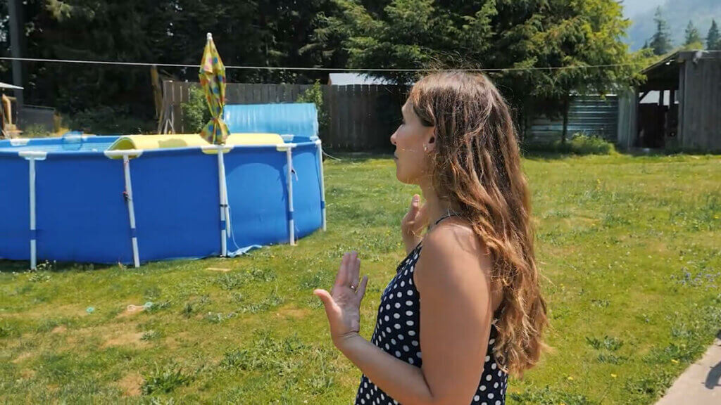 A woman gesturing to an above ground pool.