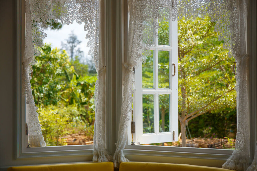 An open window with sheer curtains looking out into a yard.