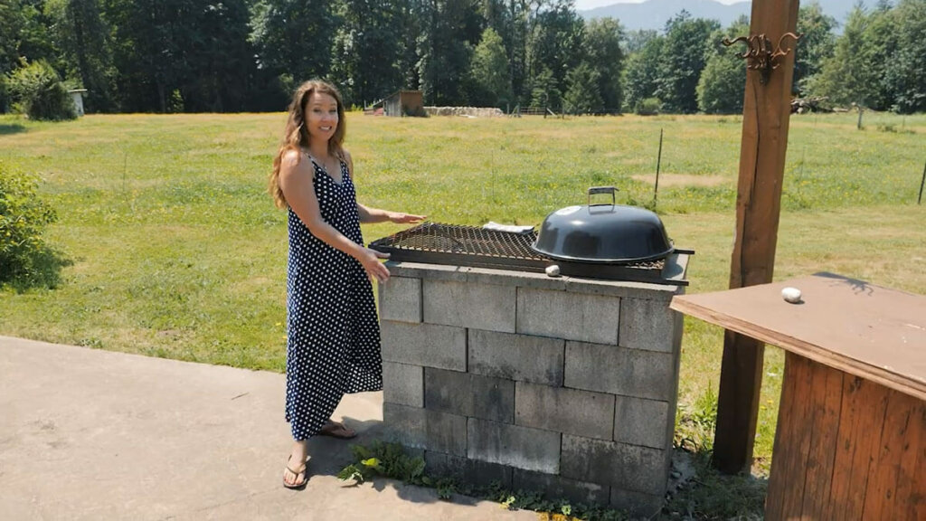 A woman standing beside an outdoor kitchen and cinderblock bbq.