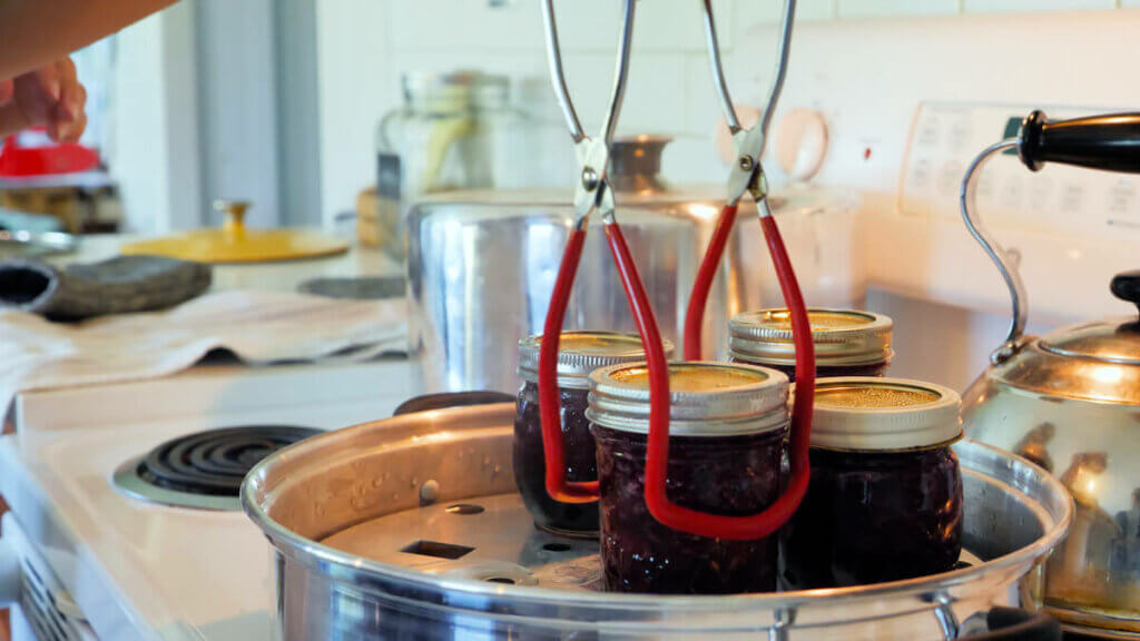 Jar lifters lifting out a finished batch of cherry jam from a steam canner on a stovetop.