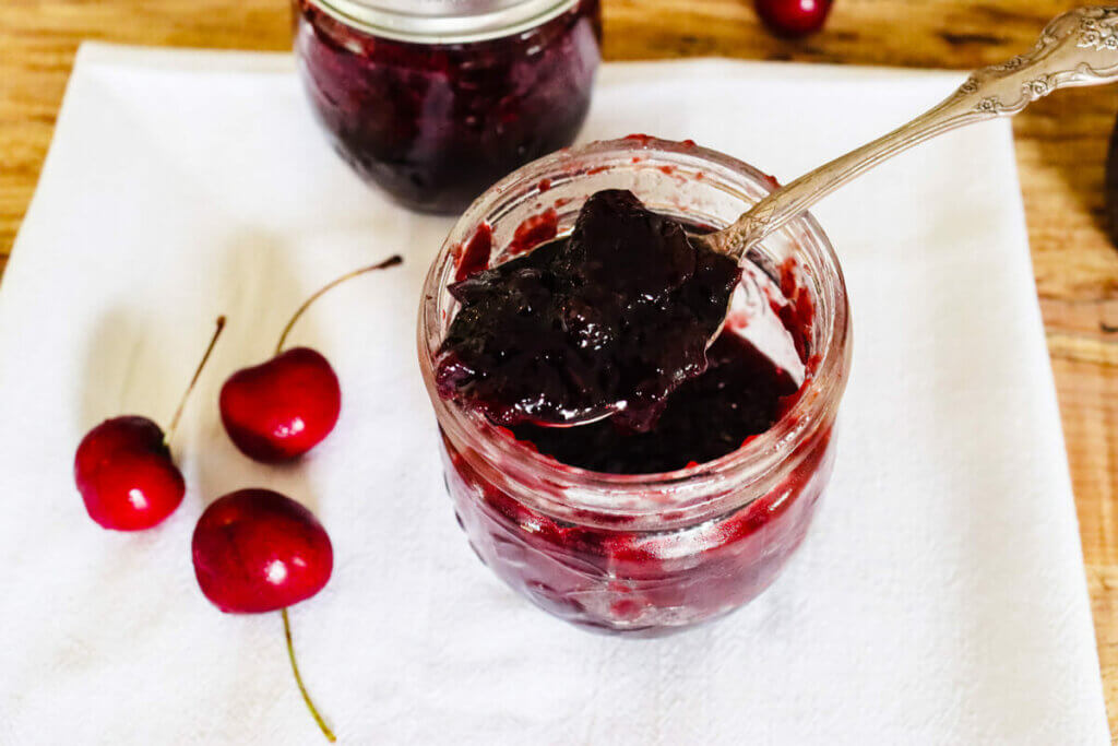 An opened jar of cherry jam with a spoonful.