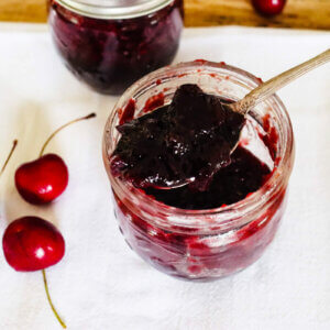 An opened jar of cherry jam with a spoonful.