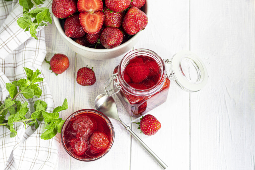 Fresh strawberries in a white bowl with strawberries in a glass.