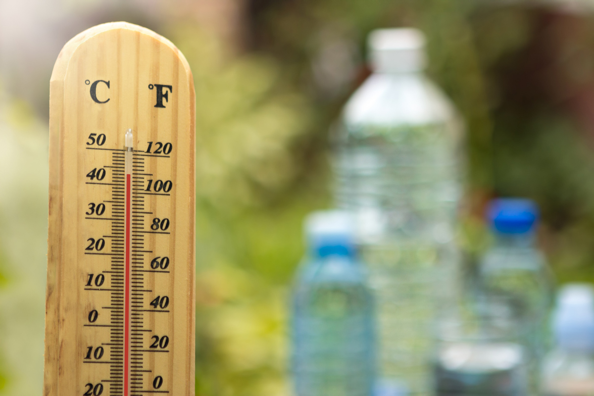 An outdoor thermometer with bottles of water in the background.