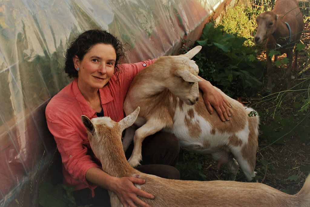 Image of a woman sitting on the ground with two goats.