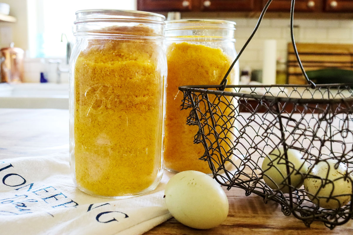 Two quart mason jars filled with freeze dried eggs sitting on a counter with a basket of eggs beside it.