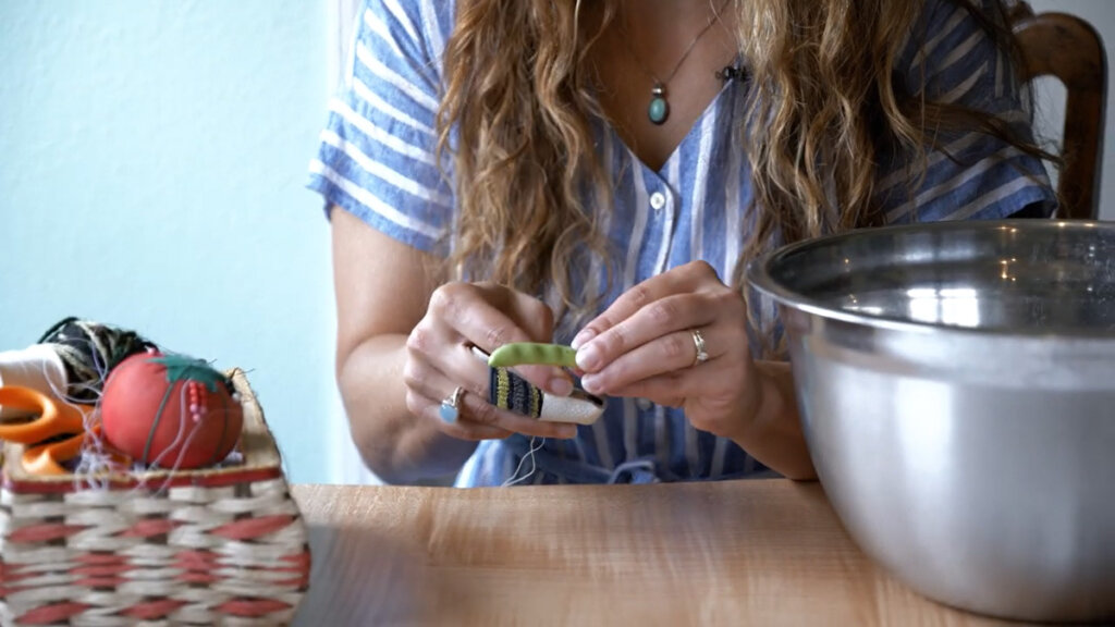 A woman poking a needle through a green bean to make leather britches.