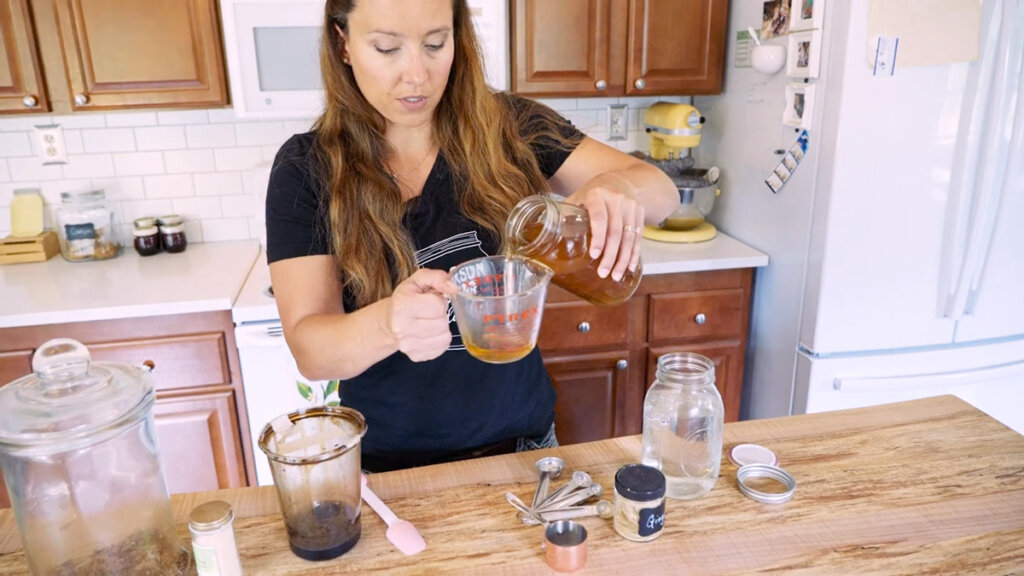 A woman measuring out apple cider vinegar for ginger water.