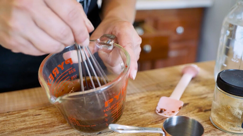 A pyrex mixing bowl with ginger water ingredients being whisked together.